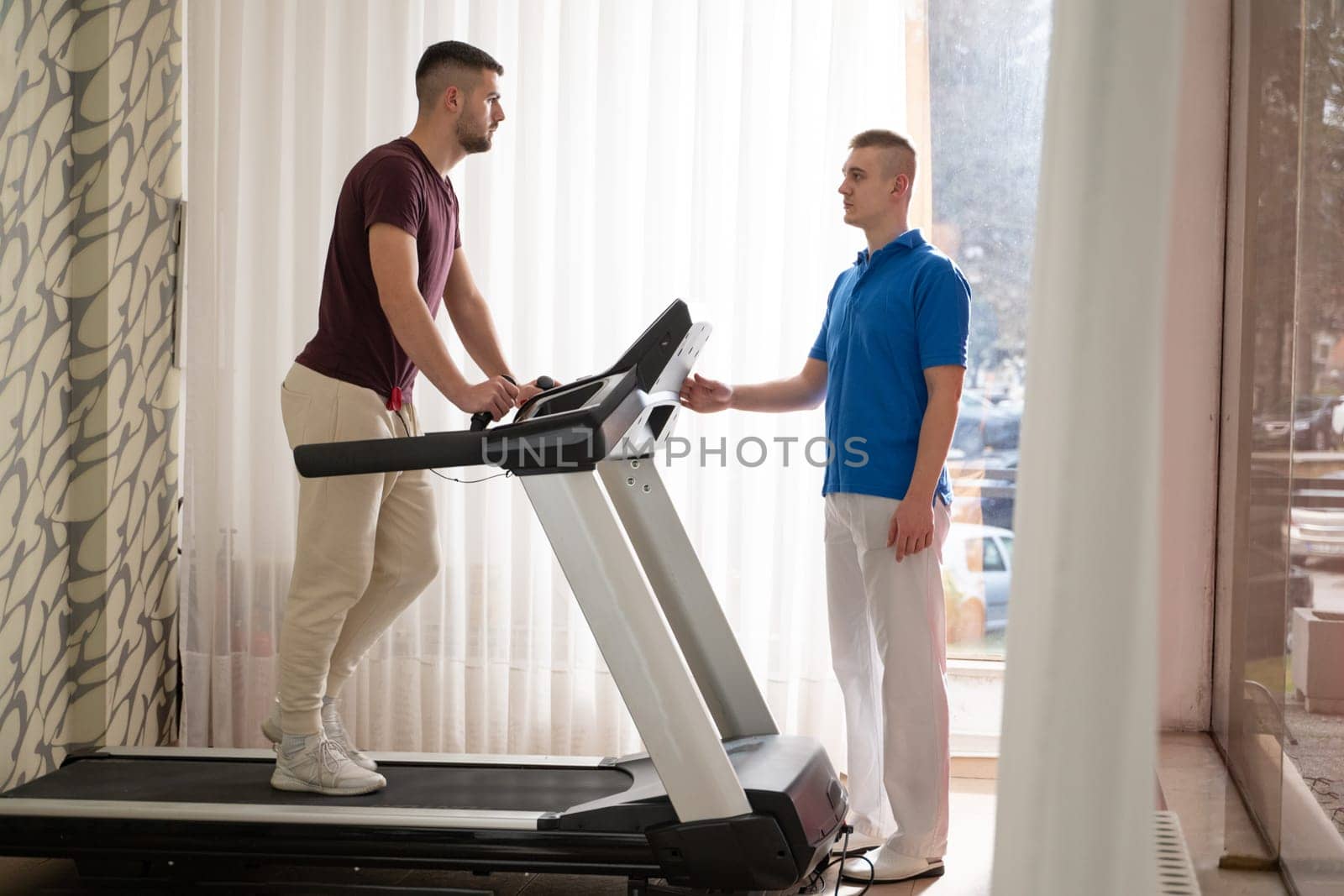 Man undergoing physical therapy with trainer assistance on a treadmill indoors.