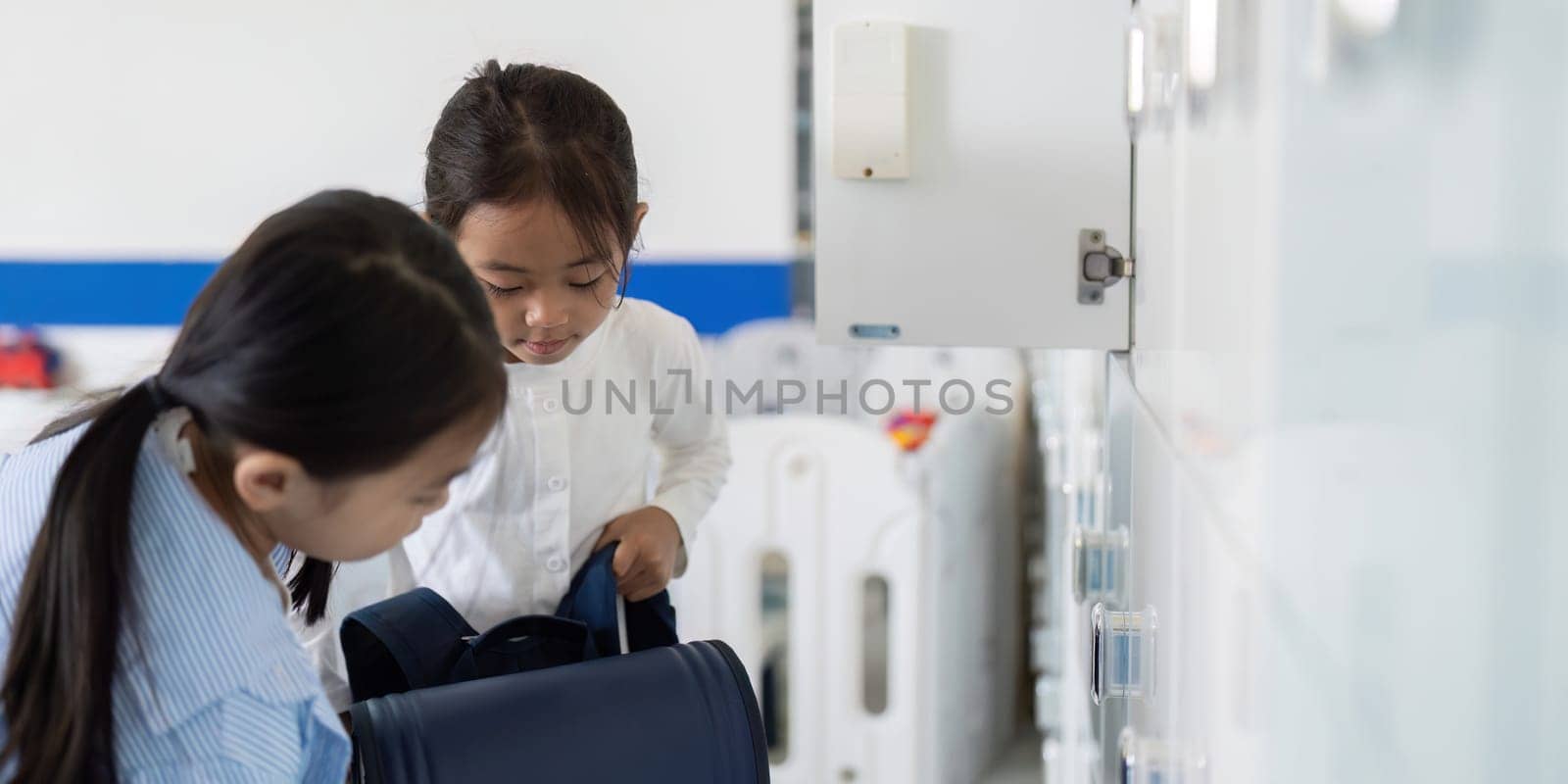 Two girls are organizing their backpacks at school lockers, demonstrating teamwork and preparation for the day.