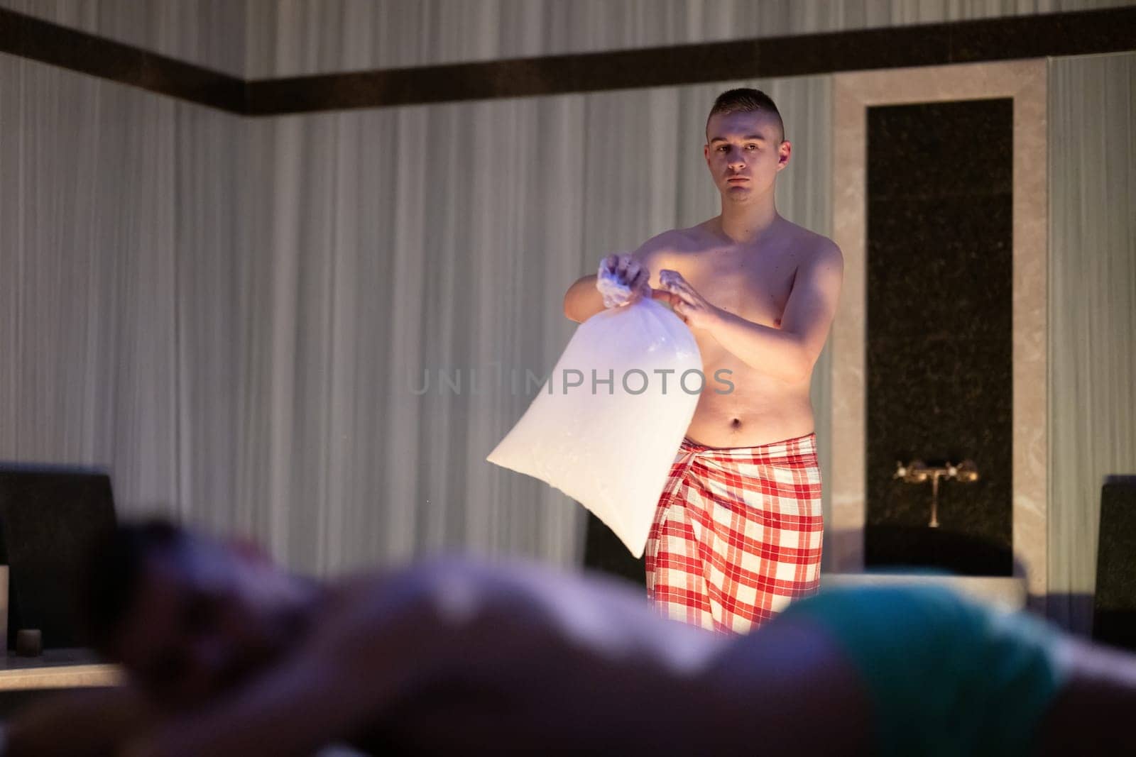 Hamam Attendant with Towel.Young male attendant preparing towel in traditional Turkish bath, standing near client