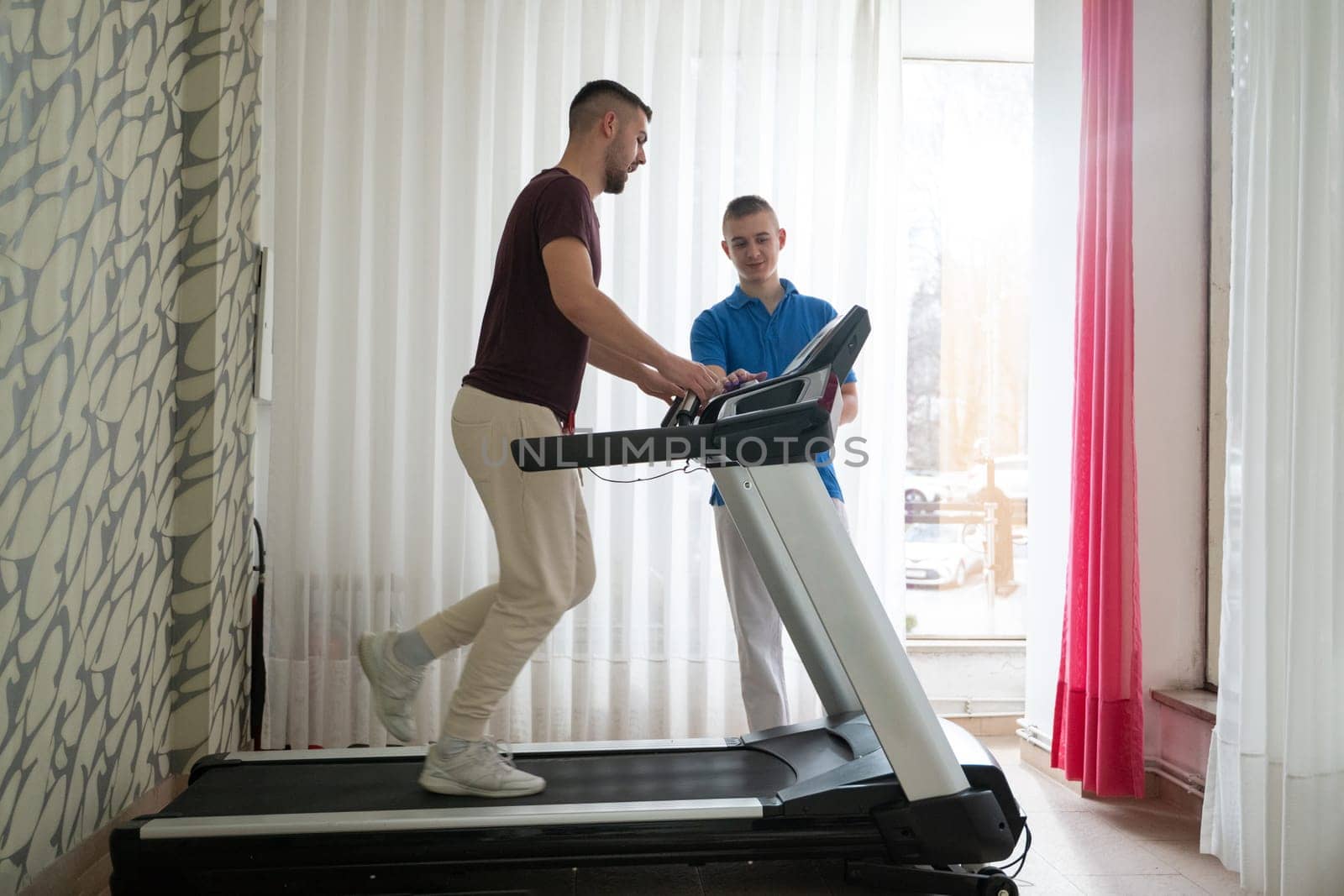 Man undergoing physical therapy with trainer assistance on a treadmill indoors.