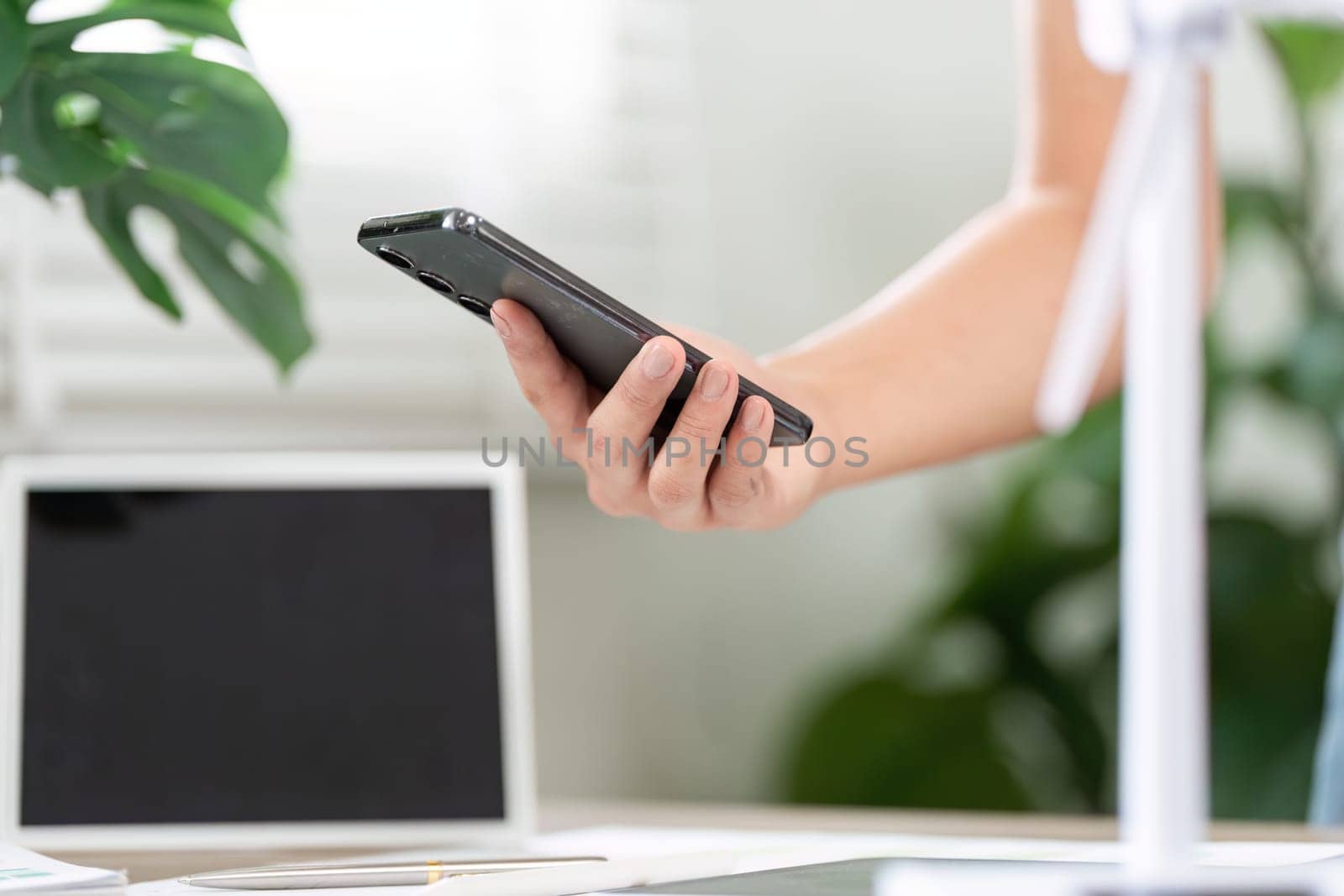 A close-up of a hand holding a smartphone, symbolizing digital communication and sustainable business practices in an office.