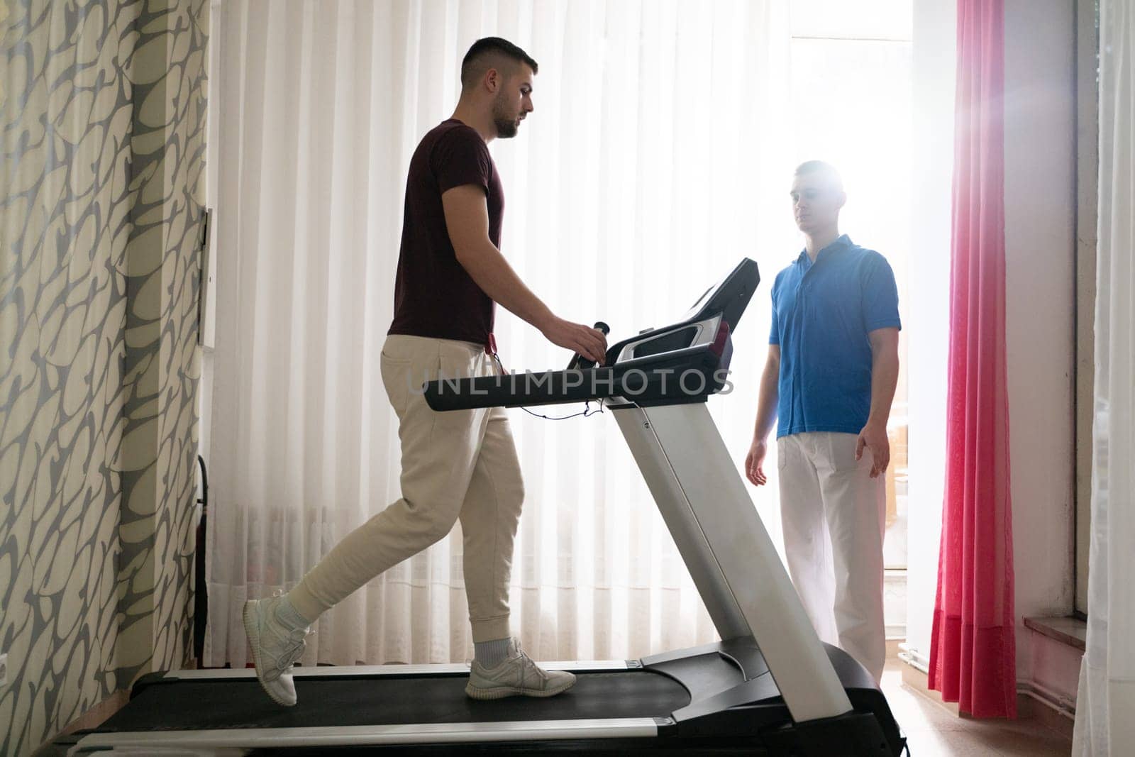 Man undergoing physical therapy with trainer assistance on a treadmill indoors.