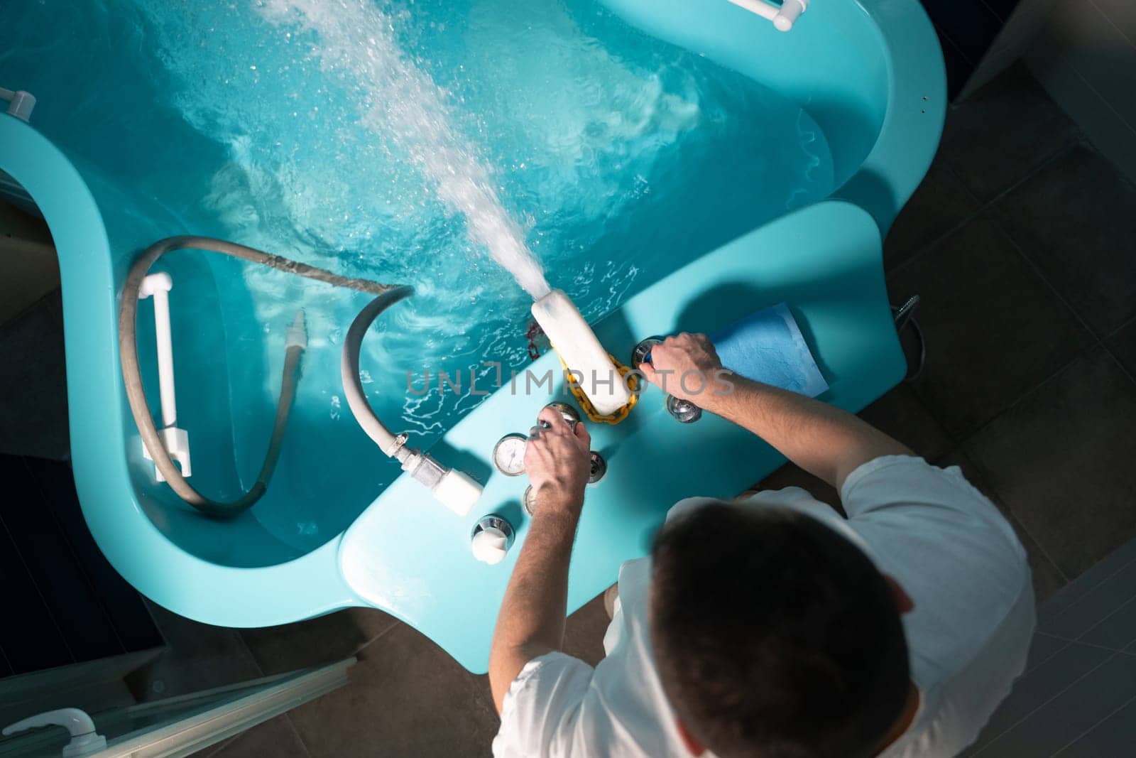 A therapist preparing a hydrotherapy bathtub for a patient inside a tiled wellness room. Spa Therapist Adjusting Tub