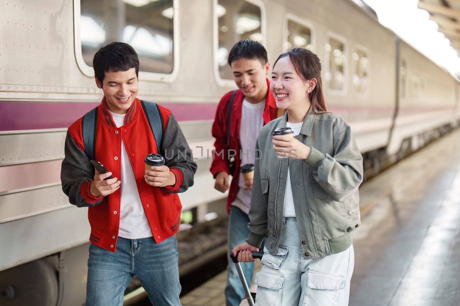 A group of friends walking and chatting at the train station, enjoying their coffee and the excitement of travel.