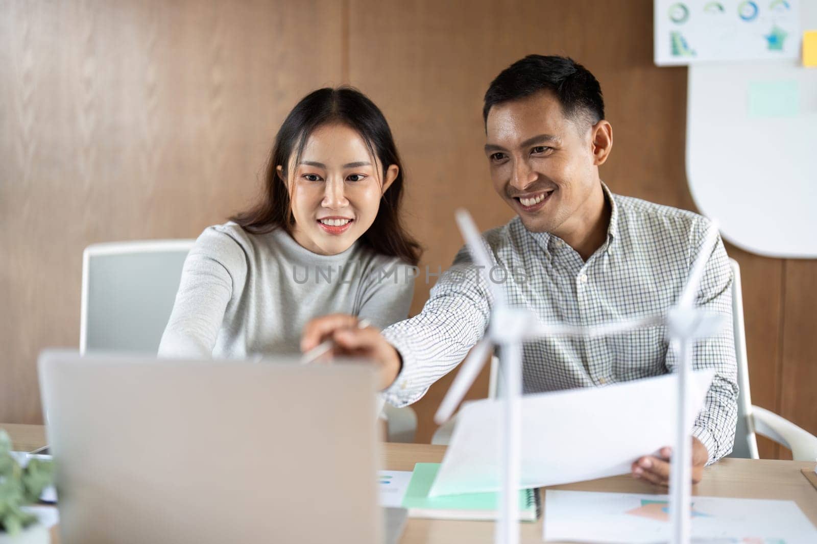 A man and woman enthusiastically discuss their wind energy project, sharing ideas and reviewing plans in a collaborative office environment.