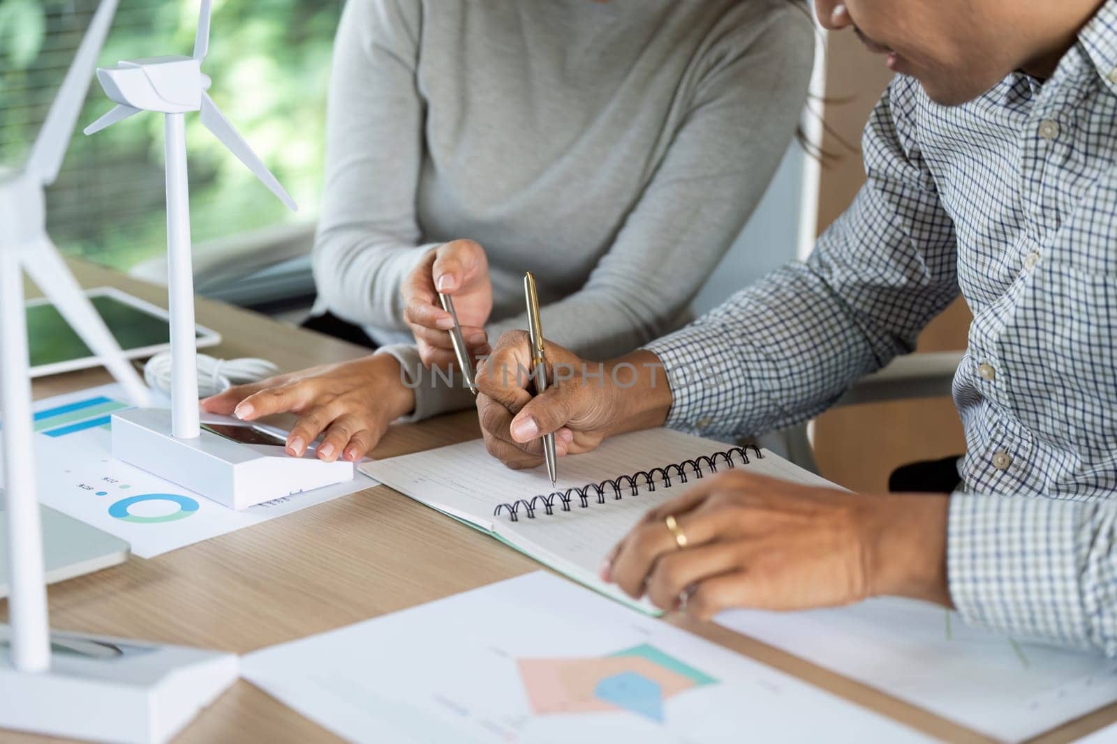Two professionals engage in a discussion about renewable energy solutions, taking notes and analyzing data.