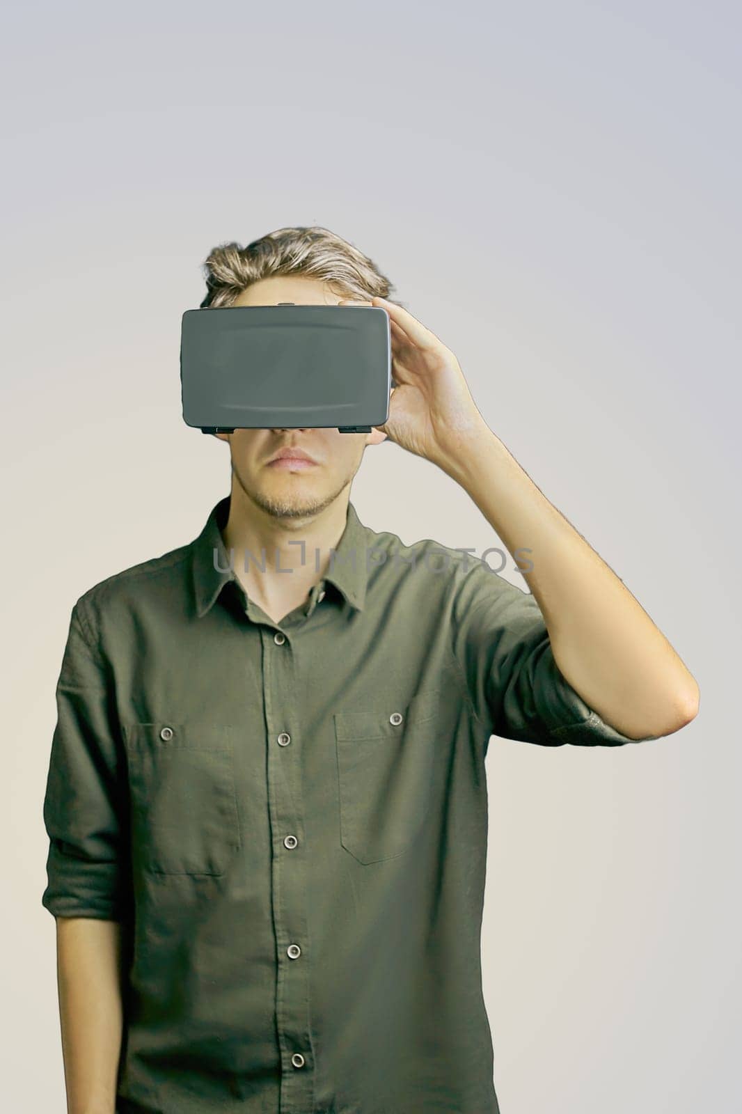 Young man in a shirt uses virtual reality glasses on the light grey background
