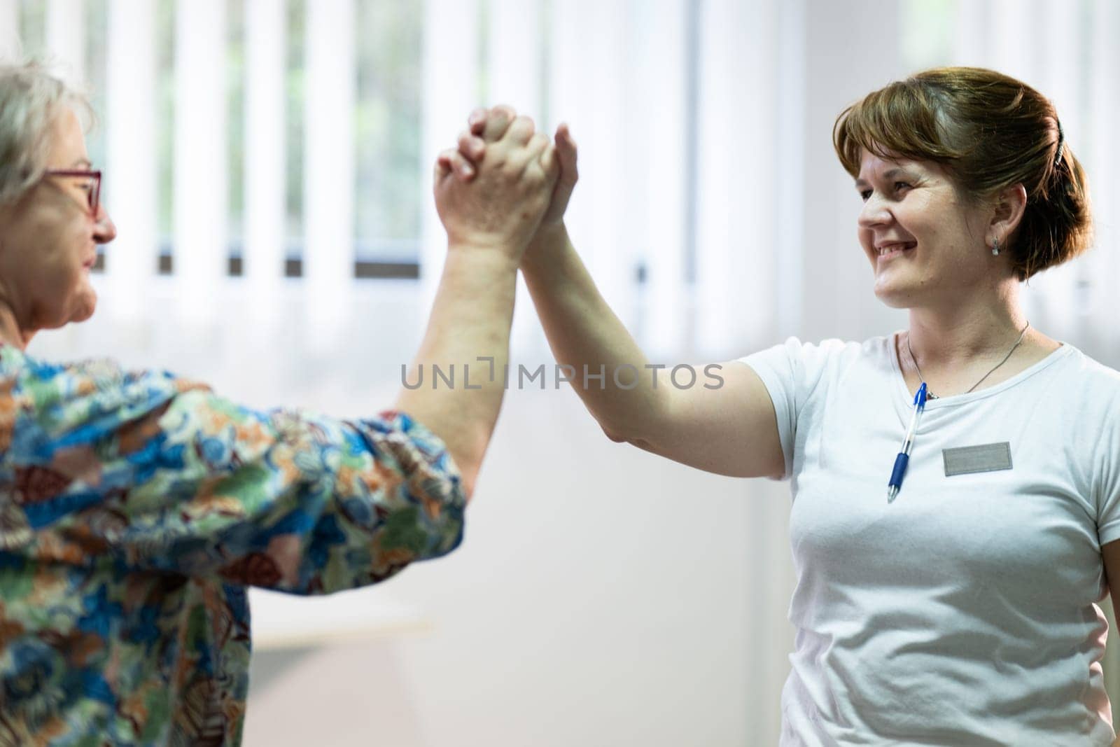 Senior woman doing physical exercises with the help of a smiling therapist. Concept of elderly rehabilitation and movement recovery.