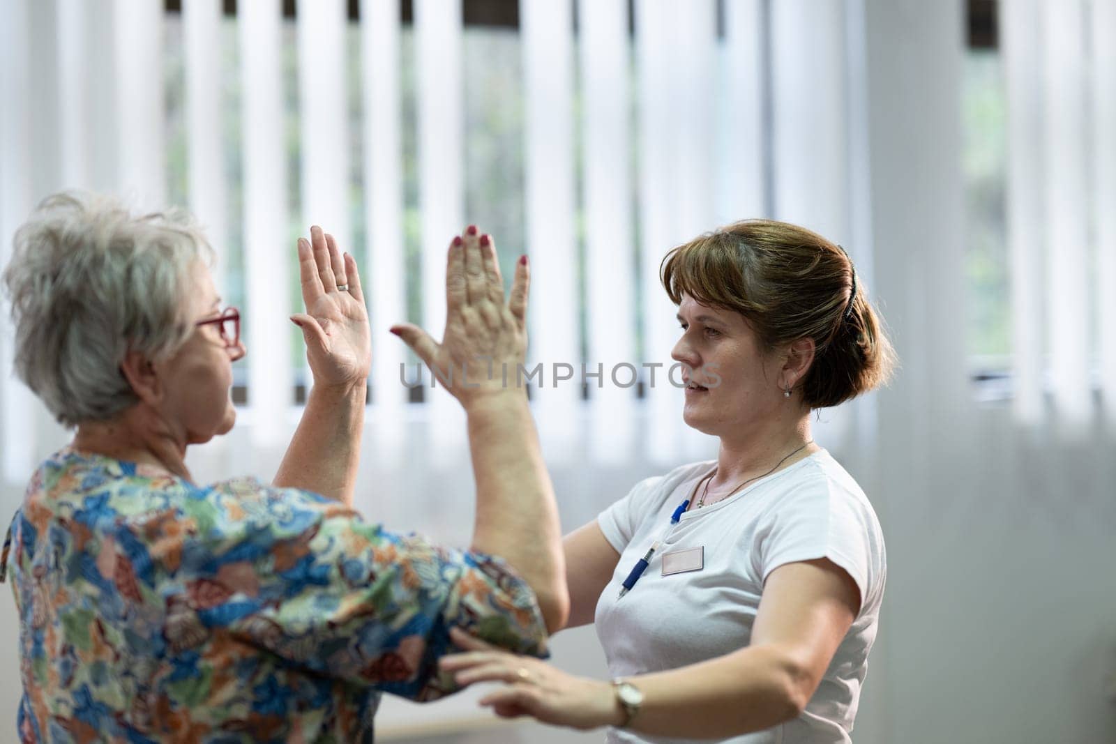 Senior woman doing physical exercises with the help of a smiling therapist. Concept of elderly rehabilitation and movement recovery.