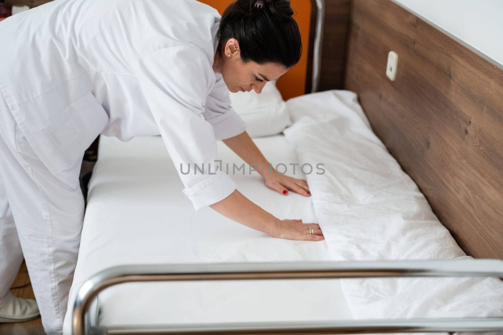 Two nurses in uniforms cleaning and organizing a hospital room by changing the bed linens and ensuring a hygienic environment for patients
