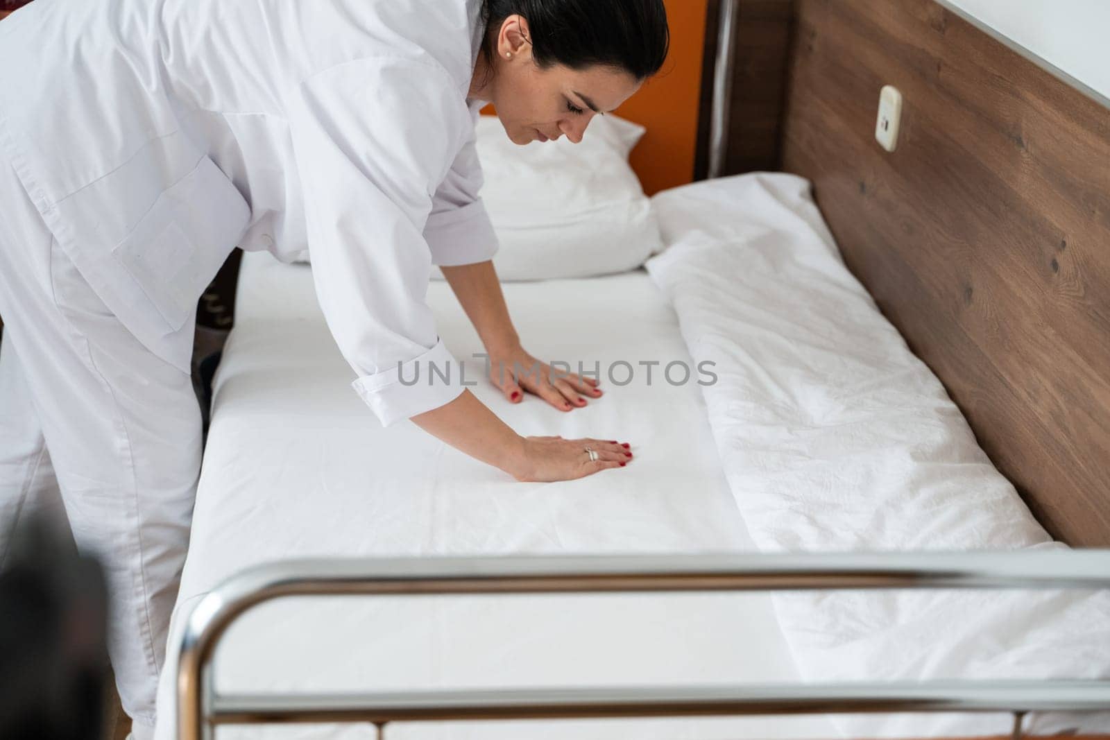 Two nurses in uniforms cleaning and organizing a hospital room by changing the bed linens and ensuring a hygienic environment for patients