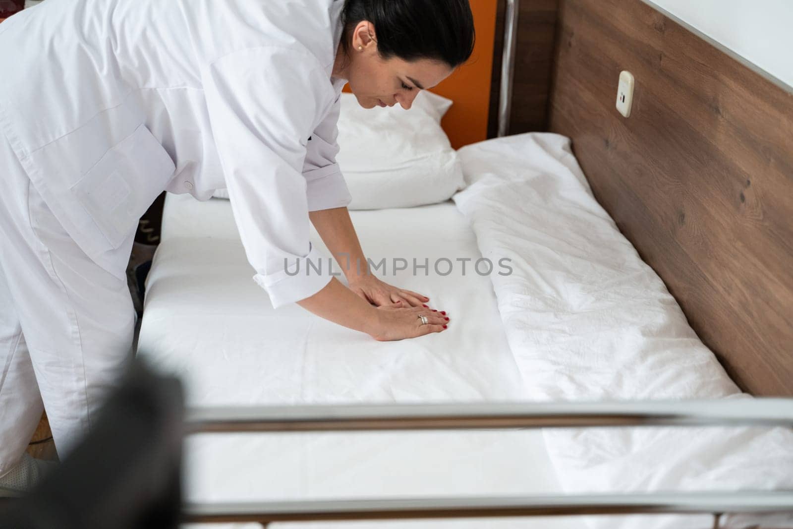 Two nurses in uniforms cleaning and organizing a hospital room by changing the bed linens and ensuring a hygienic environment for patients