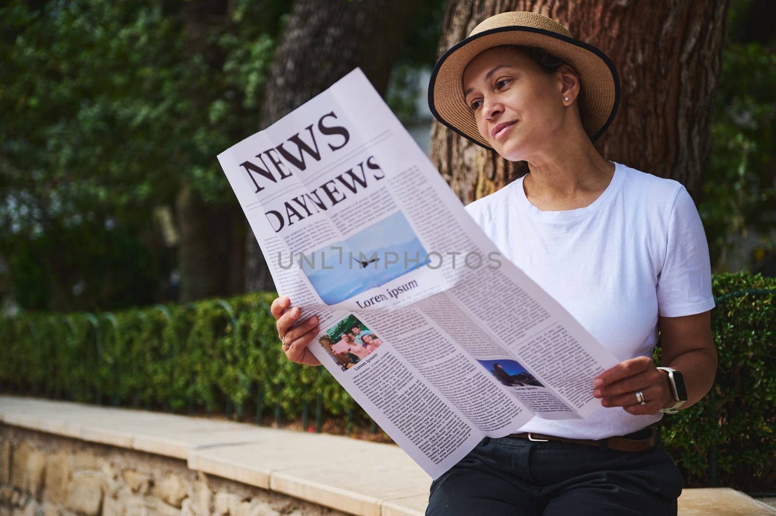 Woman enjoying a moment of relaxation in a calm outdoor park while reading a printed newspaper. Pleasant greenery and natural environment enhance the tranquil atmosphere.