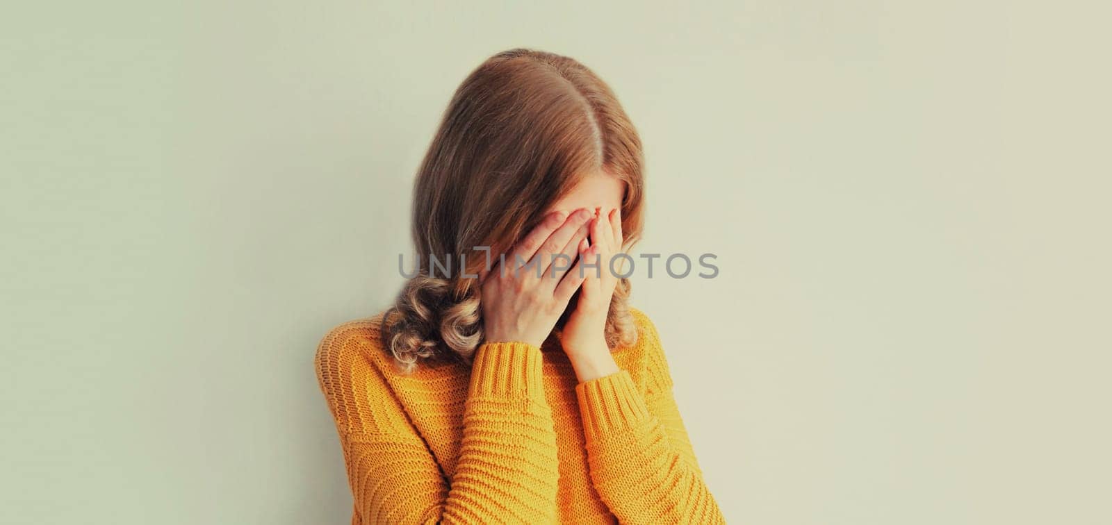 Upset sad crying woman covers her eyes and face with her hands while experiencing depression, stress, fatigue, mental suffering