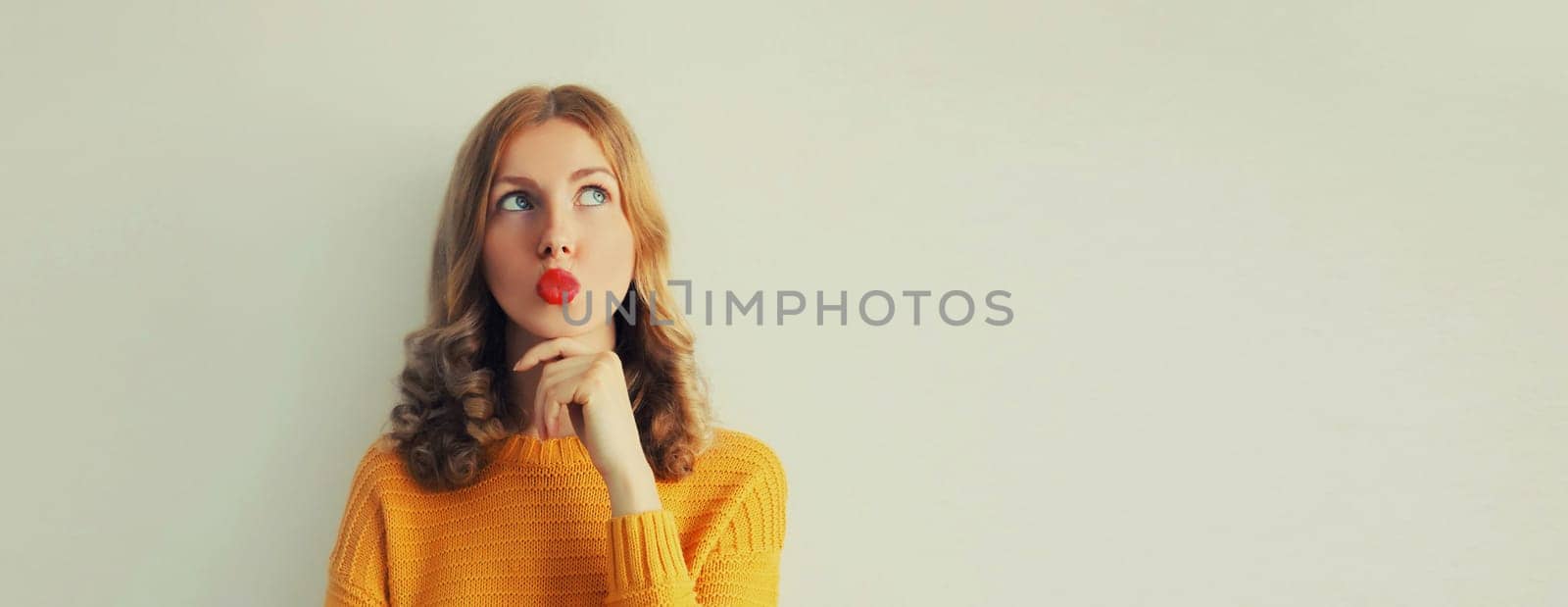 Portrait of beautiful pensive caucasian young woman thinks looking up on studio background, girl blowing her lips with red lipstick, blank copy space