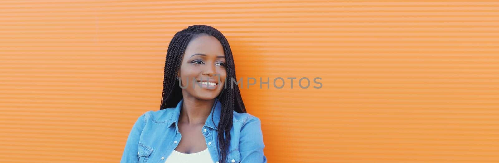 Portrait of happy confident smiling young african woman, successful black girl looking away standing on an orange background
