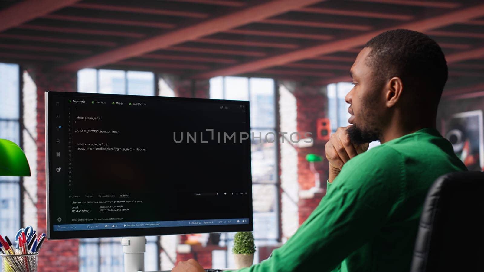Black technician in home office looks at UI on computer monitor, typing and executing programming code. IT worker using coding application to write and test code in modern apartment. Camera A.