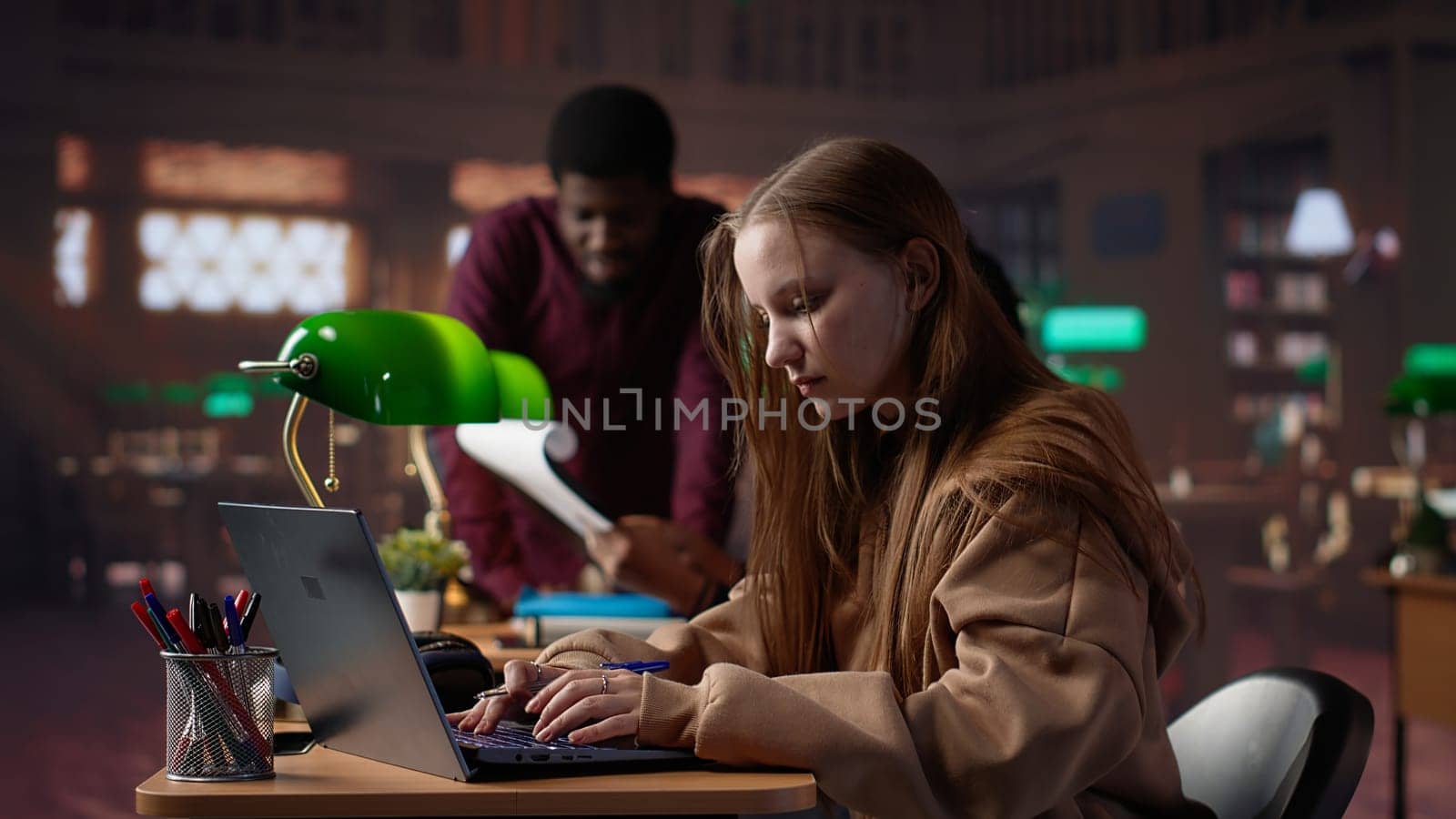 College student captivated by literature assignment at the academic library on campus, working on bachelor degree paperwork. Uses primary source materials from the database. Camera A.