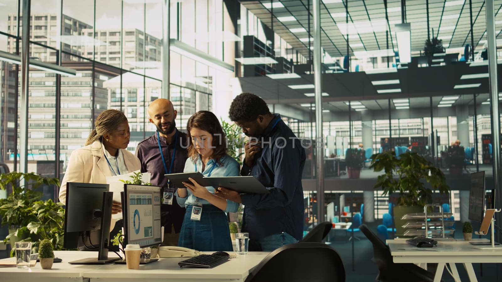 Multiethnic coworkers looking over revenue figures on tablet in diverse office. Multiracial colleagues doing brainstorming, comparing company statistical numbers, working hard to finish job, camera B