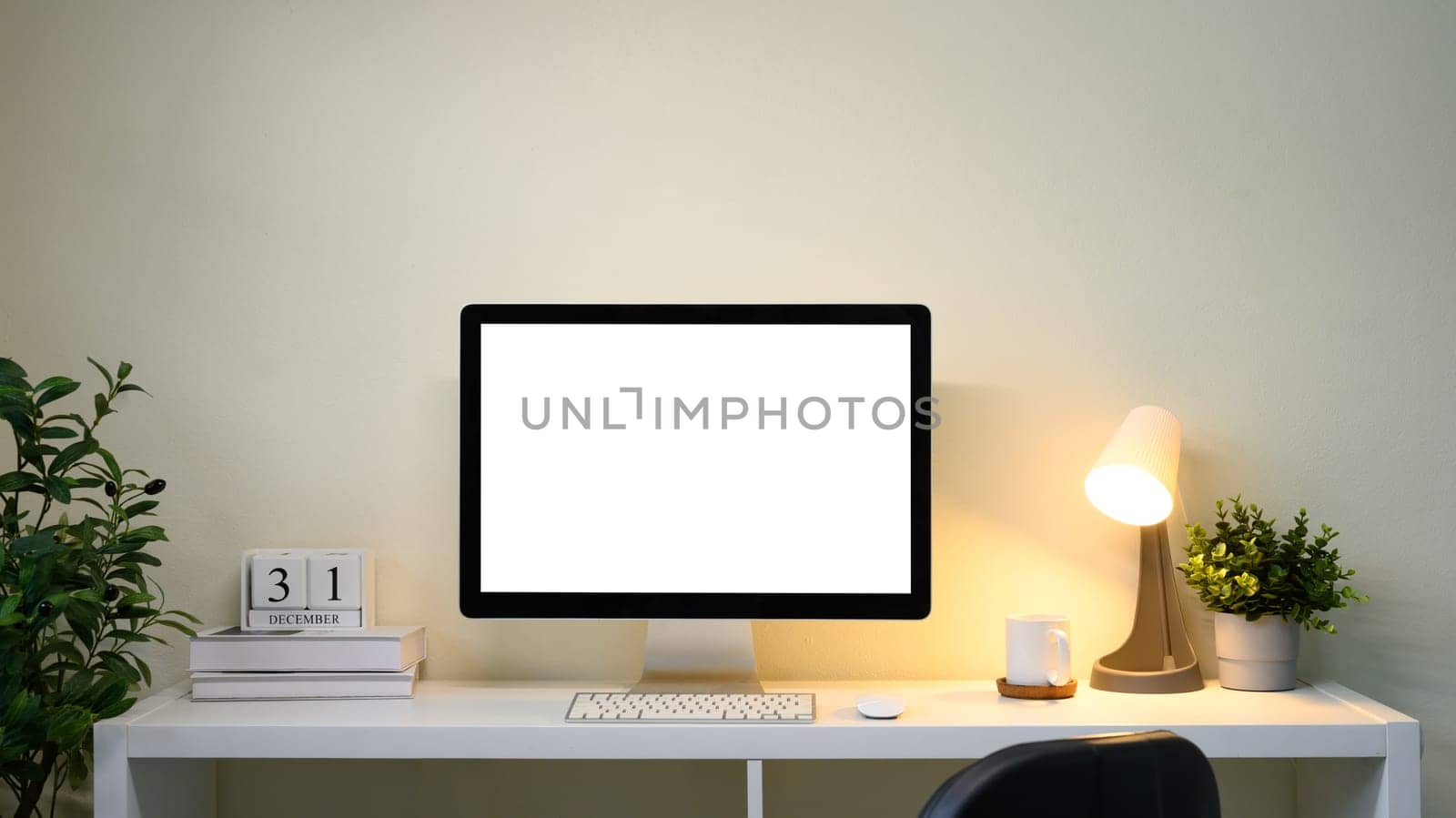 Blank screen desktop computer, calendar, desk lamp, and indoor plants.