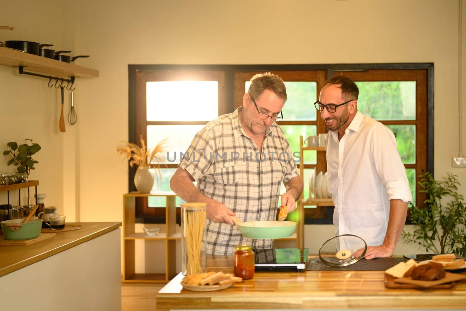 Smiling father and adult son preparing a pasta meal together in a cozy home kitchen. Father day concept.