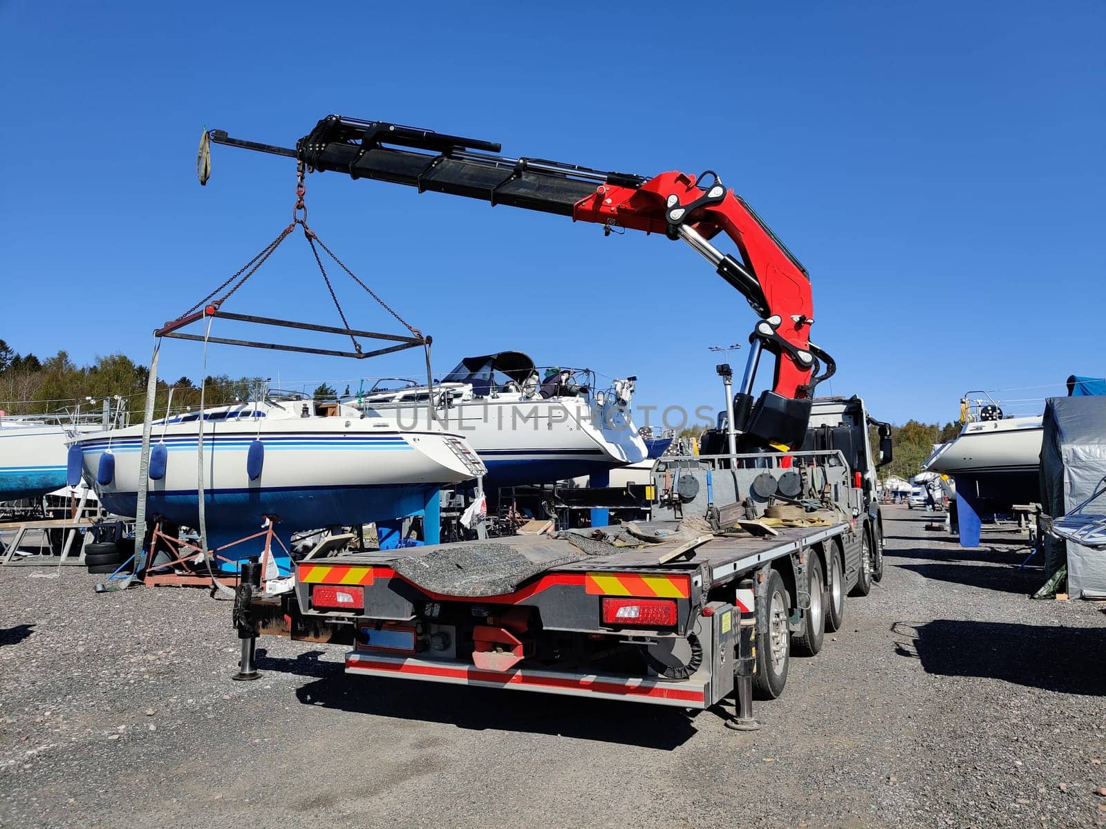 A sailboat lifted by a crane in Suomenoja harbor in Espoo, Finland. A man is holding a rope, guiding the boat as it is suspended in the air by lifting straps