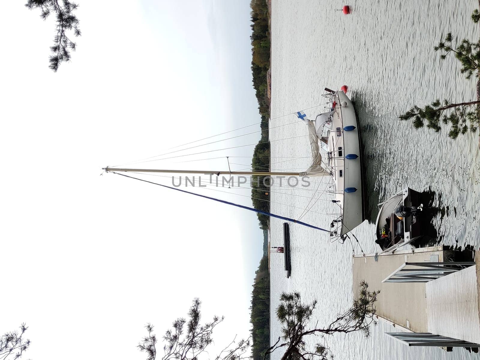 A sailboat is moored to a wooden pier in the harbor of Baltic sea, Gulf of Finland. The boat is securely tied with ropes, gently floating on calm water with finish flag