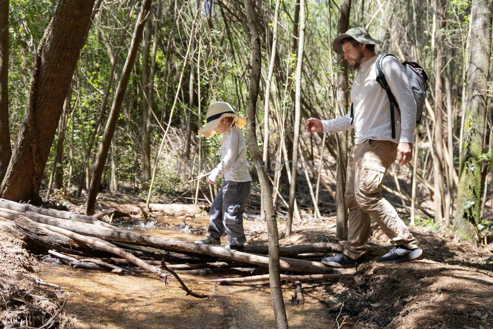 Father and son carefully crossing a small creek while hiking in a sunny forest