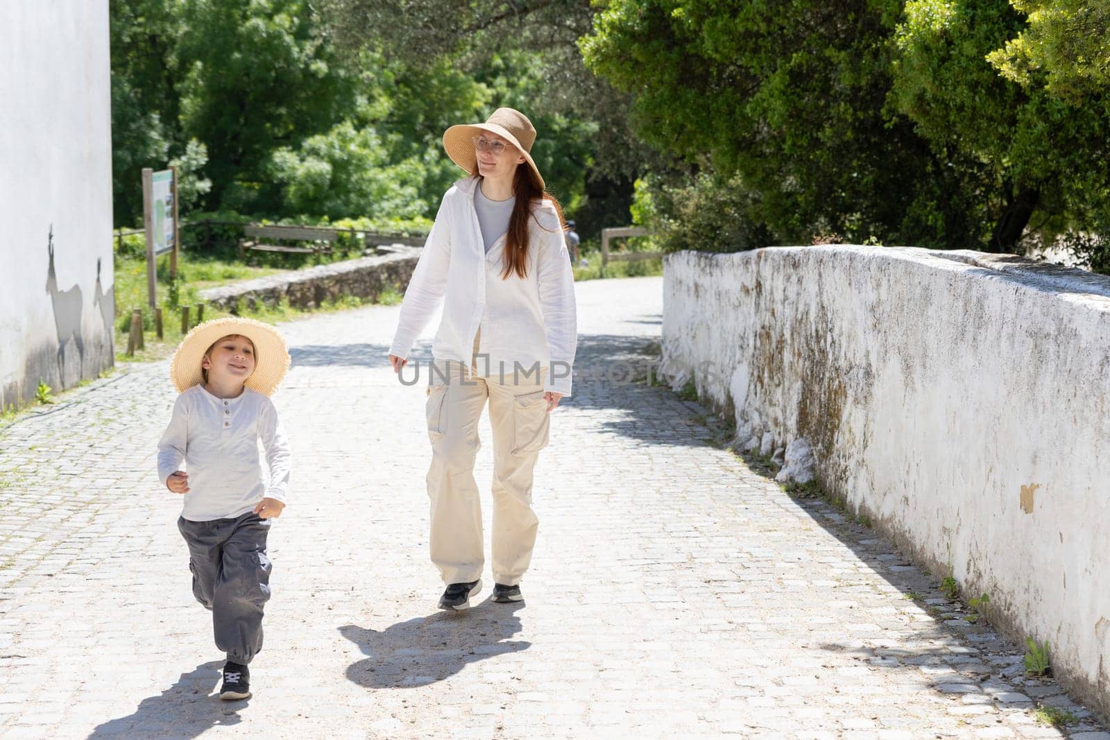 Mother and son enjoying a walk on a cobblestone street during a sunny day
