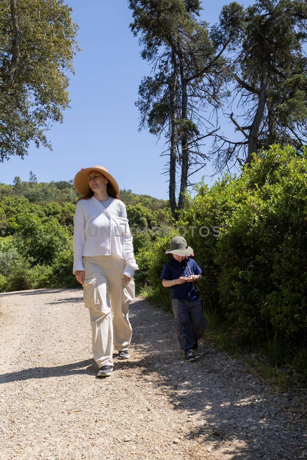 Mother and son enjoying a leisurely hike on a gravel path through a sunny nature preserve