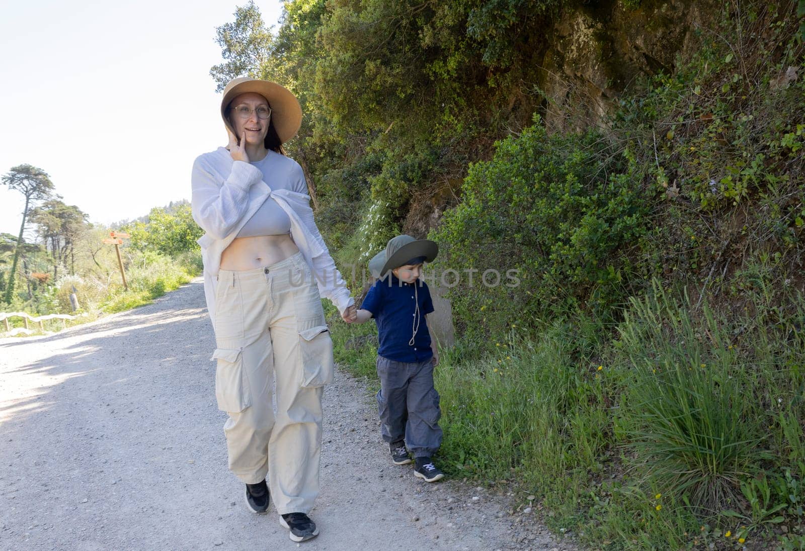 Mother talking on smartphone while walking with her son on a path through nature