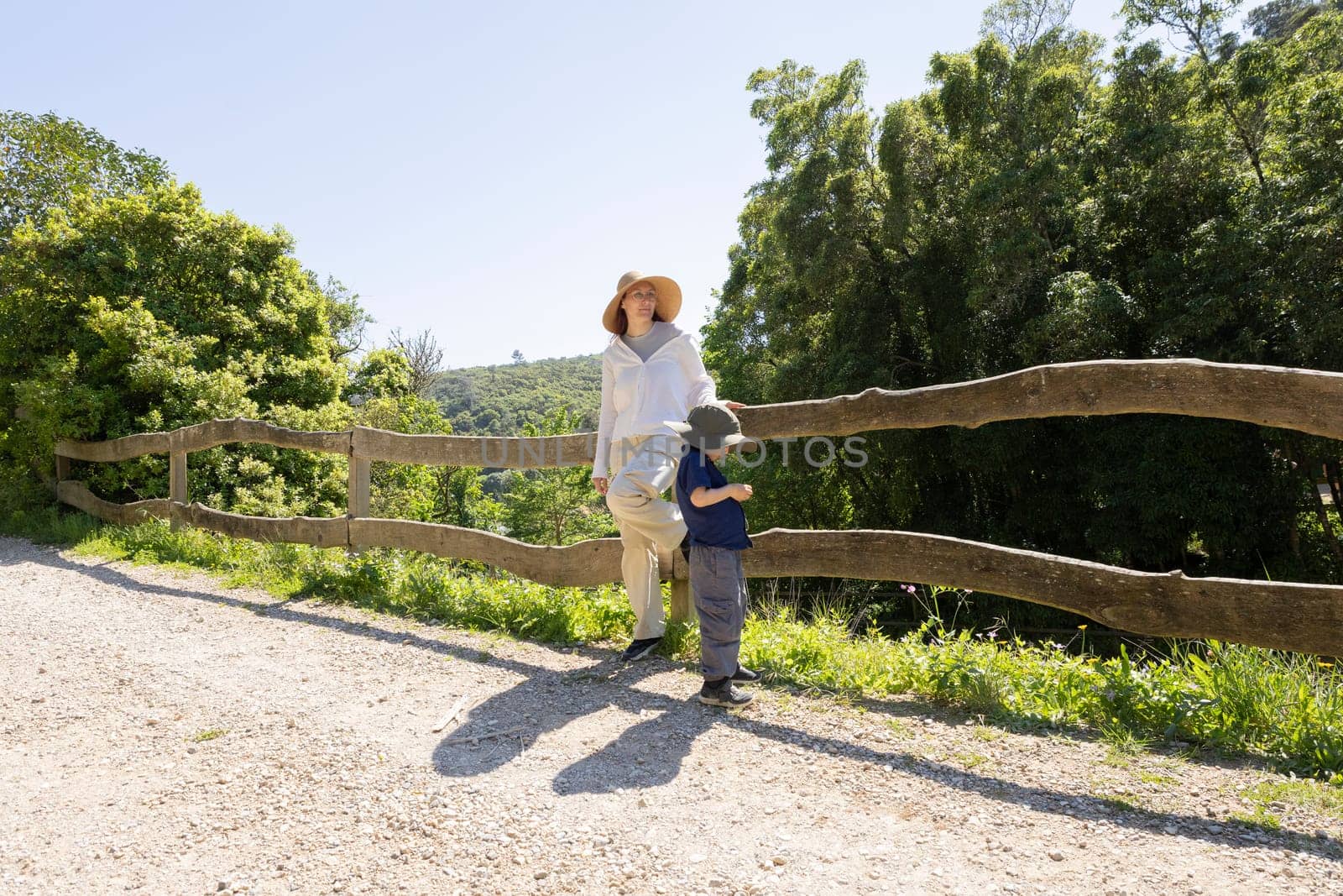 Mother and son taking a break during hike, leaning on wooden fence overlooking valley