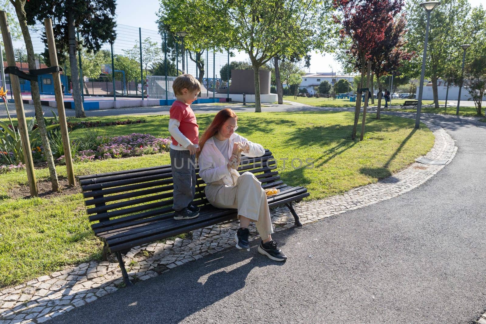 Mother disinfecting hands while sharing a snack with her son on a park bench