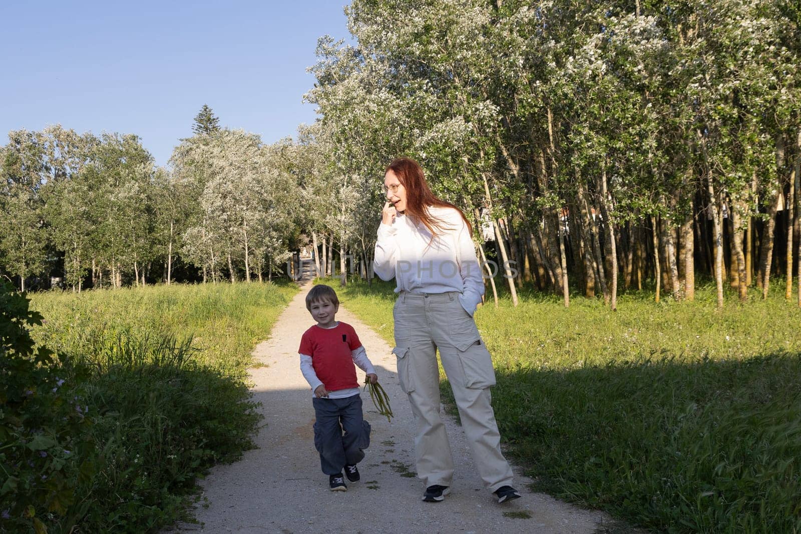 Mother and son enjoying a walk together on a sunny summer day, strolling along a path amidst lush green trees