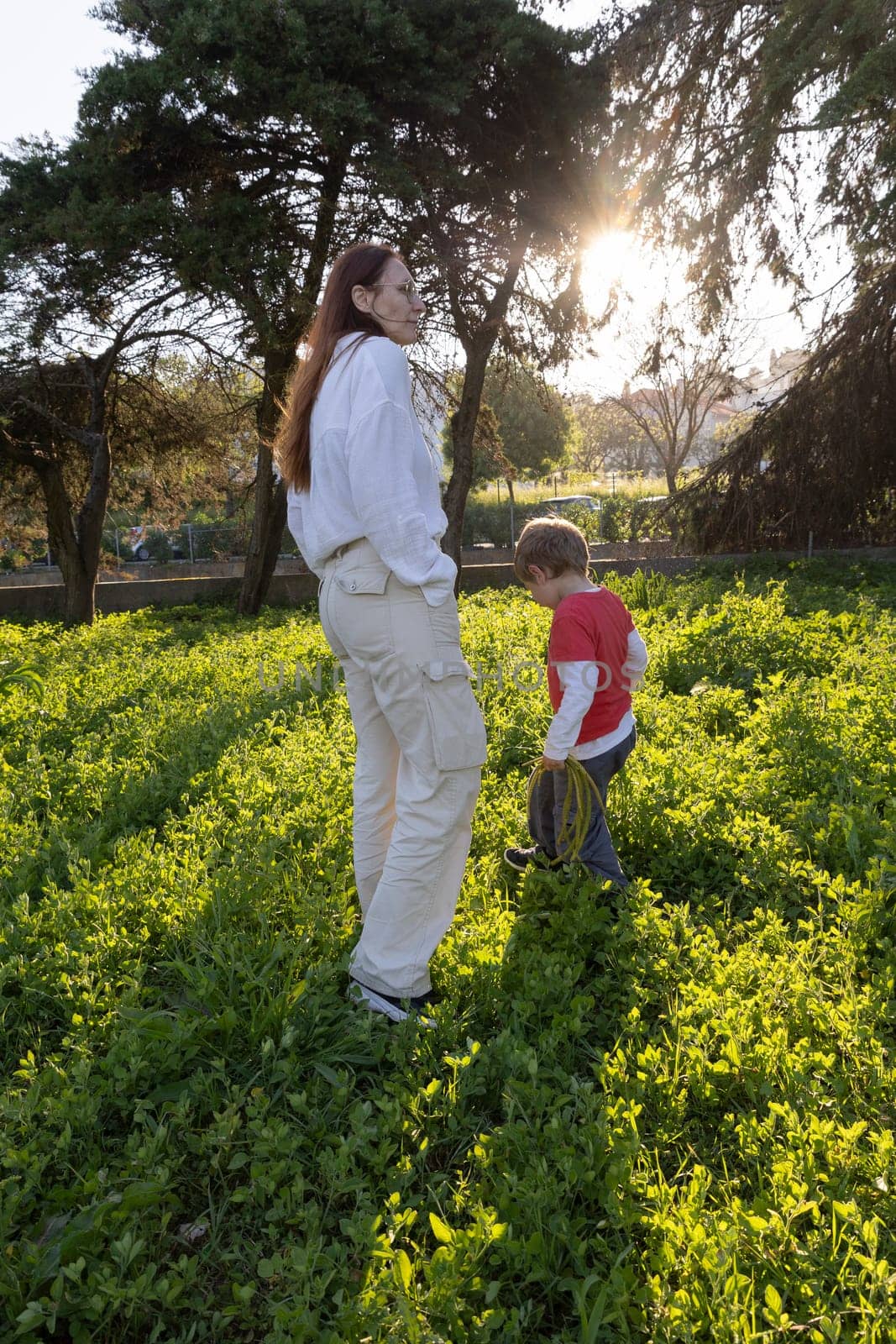 Mother and her son enjoying a walk through a green field at sunset