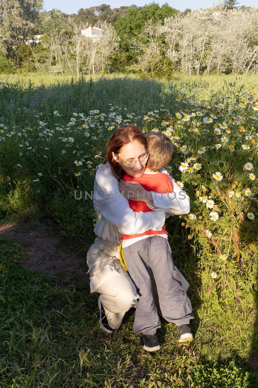 Mother and son share a tender moment in a field of daisies, enjoying the beauty of nature and the warmth of their bond