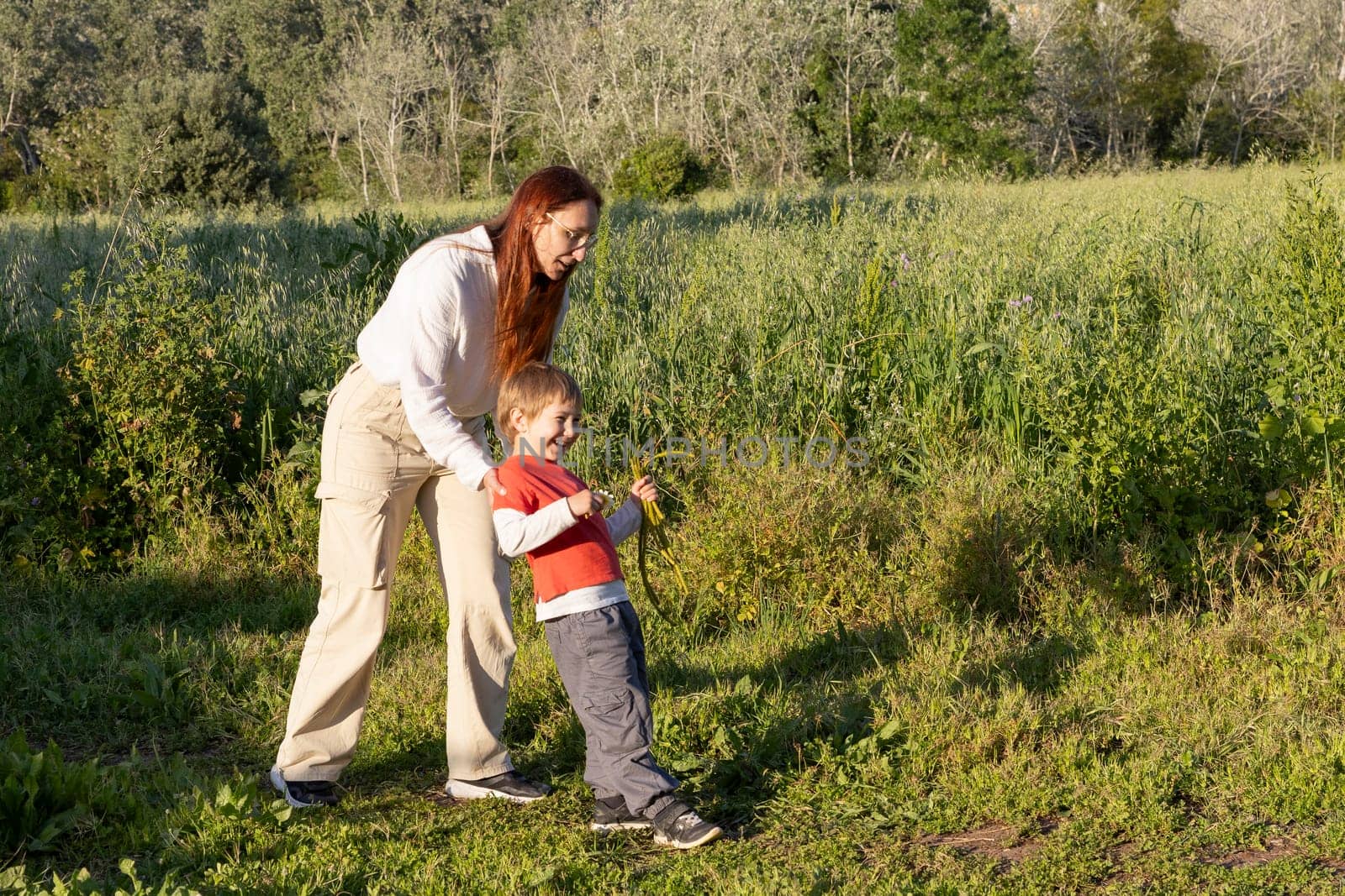 Happy mother and son having fun in a field, playing with wild plants on a sunny day