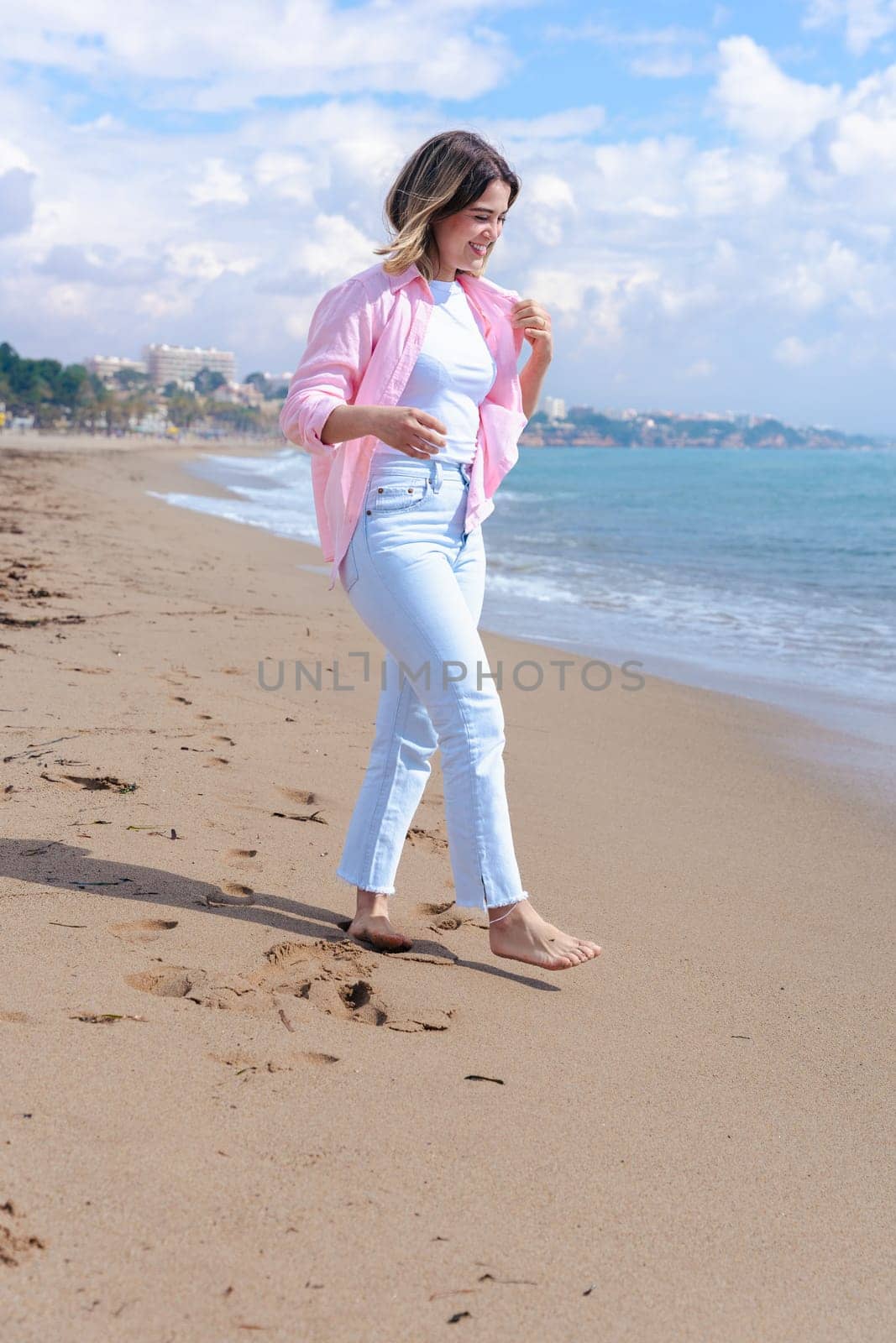 Happy young woman standing on the beach, looking at the camera with a smile. Dressed in casual clothes, she enjoys the sunny day and the relaxing ocean view in a peaceful coastal setting. Copy space