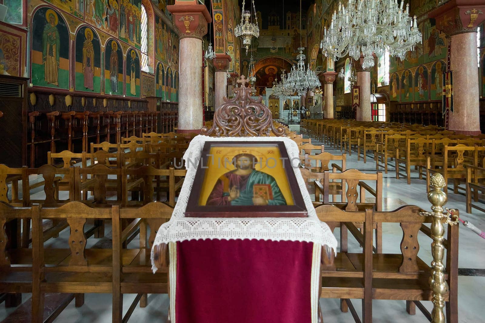 A sacred icon stands among the wooden pews, reflecting the rich artistic and spiritual tradition within the Greek Orthodox church interior.
