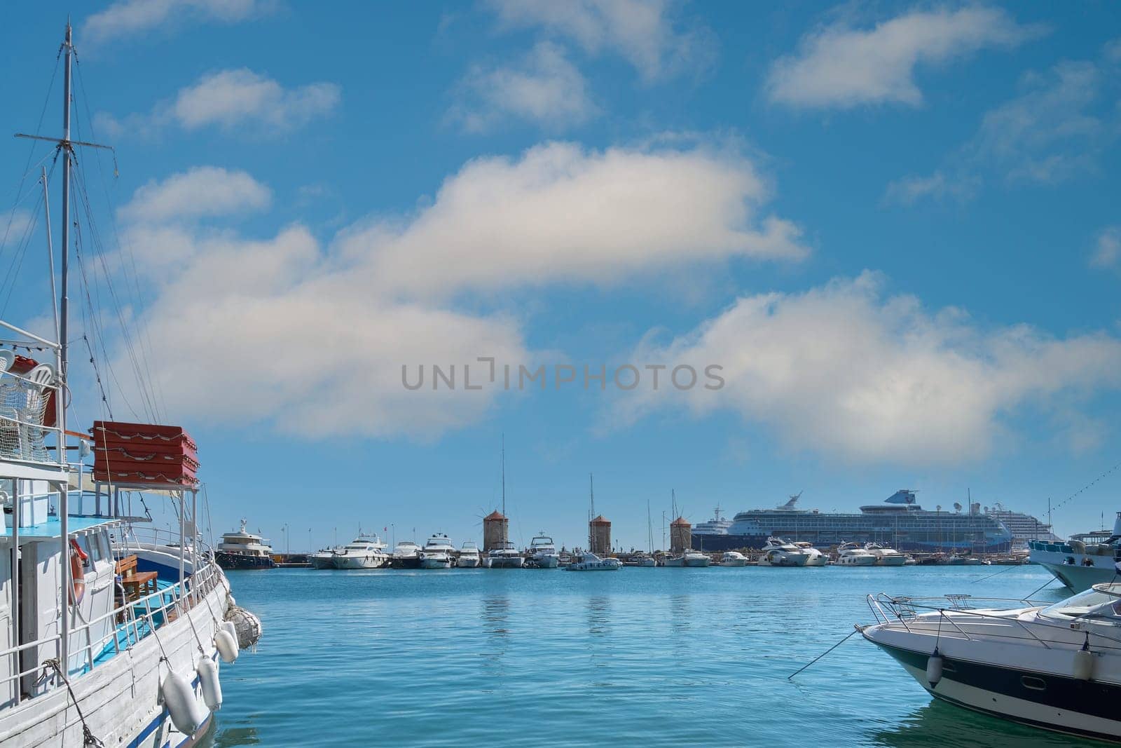 View of the iconic Mandraki harbor, with an excursion boat in the foreground and the city's historic structures in the background. Maritime heritage.