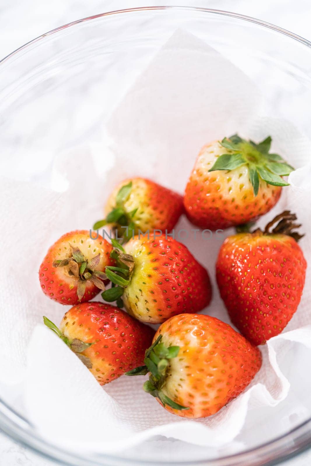 Freshly washed and dried strawberries are carefully arranged in a glass bowl lined with paper towel, ready for snacking or further use.