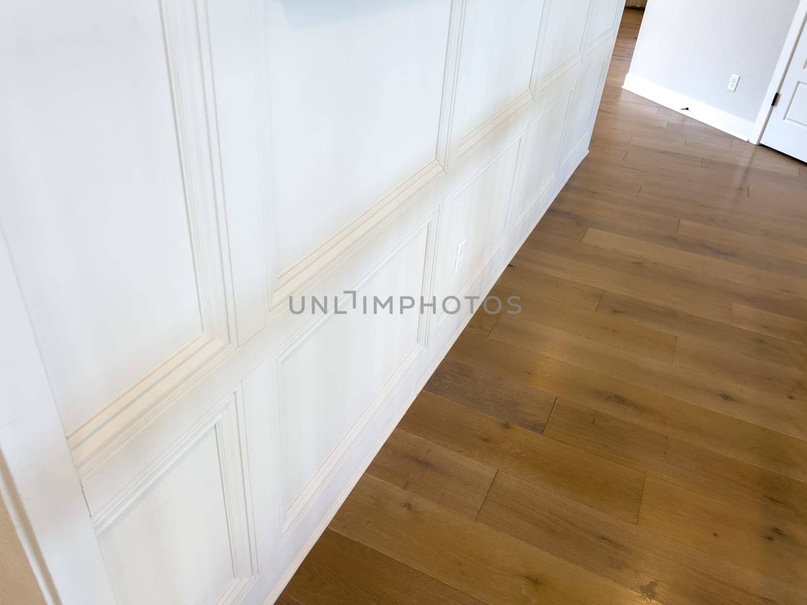 Clean interior shot showcasing a white wainscoting accent wall paired with light natural hardwood flooring. The crisp, modern design highlights architectural detail and home elegance, perfect for content related to real estate, home renovation, or interior design inspiration.