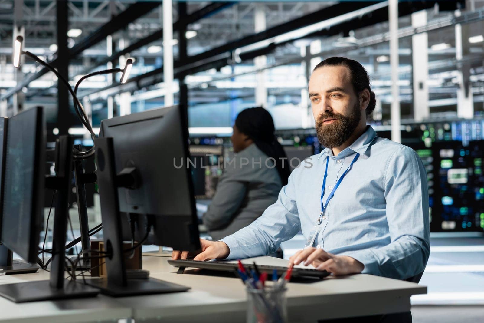 Data center programmer using PC to update servers tech, configuring gear using software tools. Server farm worker reviewing hardware analytics, ensuring reliable network operations