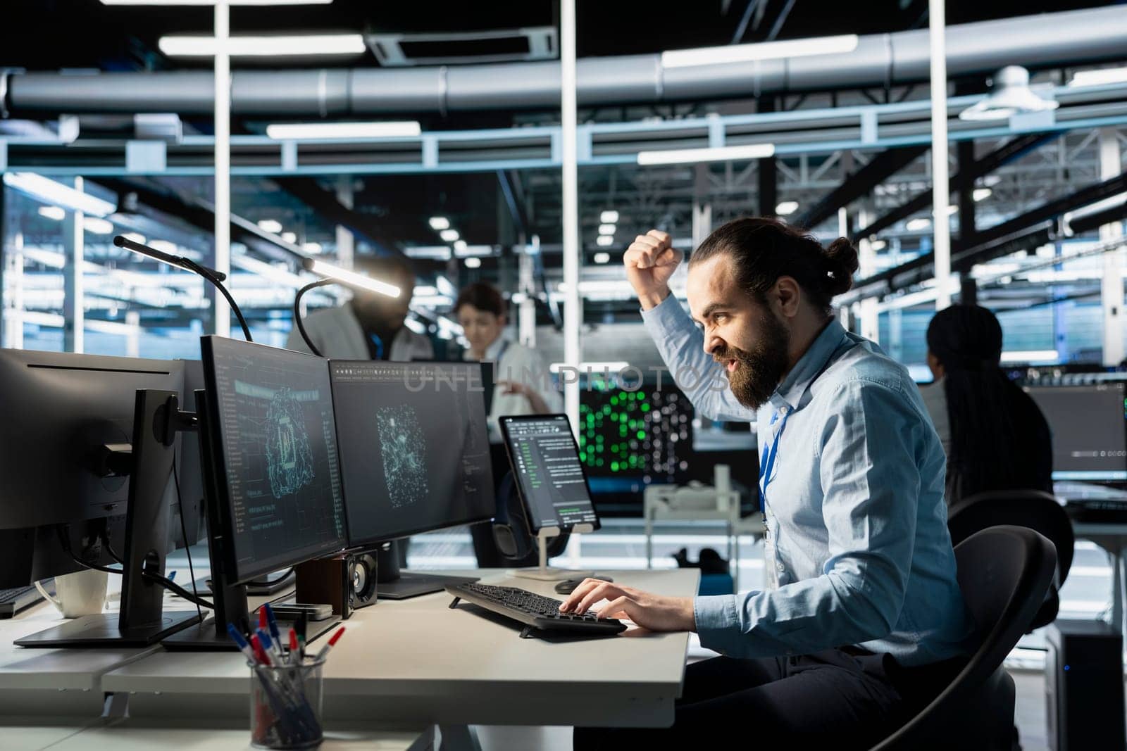 Angry software developer in data center clenching fists while looking at AI visualization interface on monitor. Frustrated technician reacting to artificial intelligence software glitches