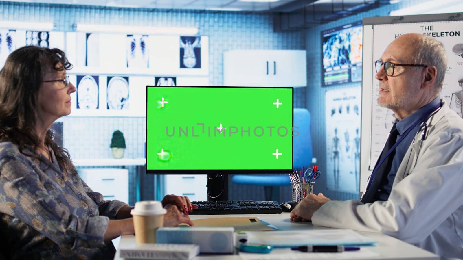 Old general practitioner discusses with female patient next to green screen, offering details from the recovery plan at the medical appointment. Medic consulting woman in cabinet. Camera B.