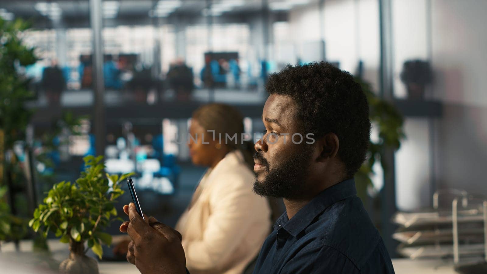 Employee in office taking break from checking documents to text friends using smartphone, relaxing. Accountant in office pausing tasks to answer messages on mobile phone, camera A