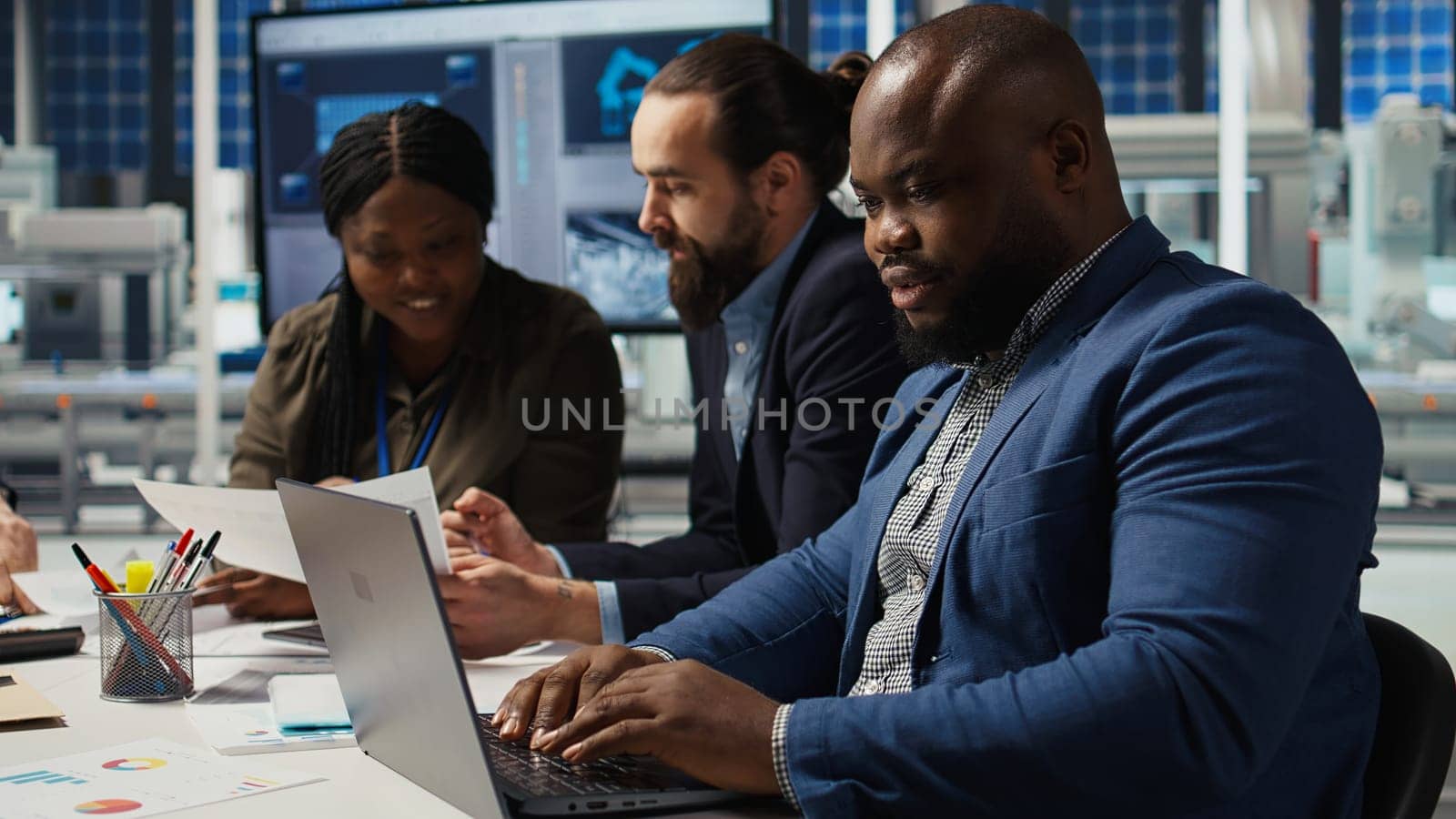 Engineers in factory office using laptop to collect performance data to refine designs for increased energy output. Photovoltaics plant experts design innovative solar cell prototypes, camera A