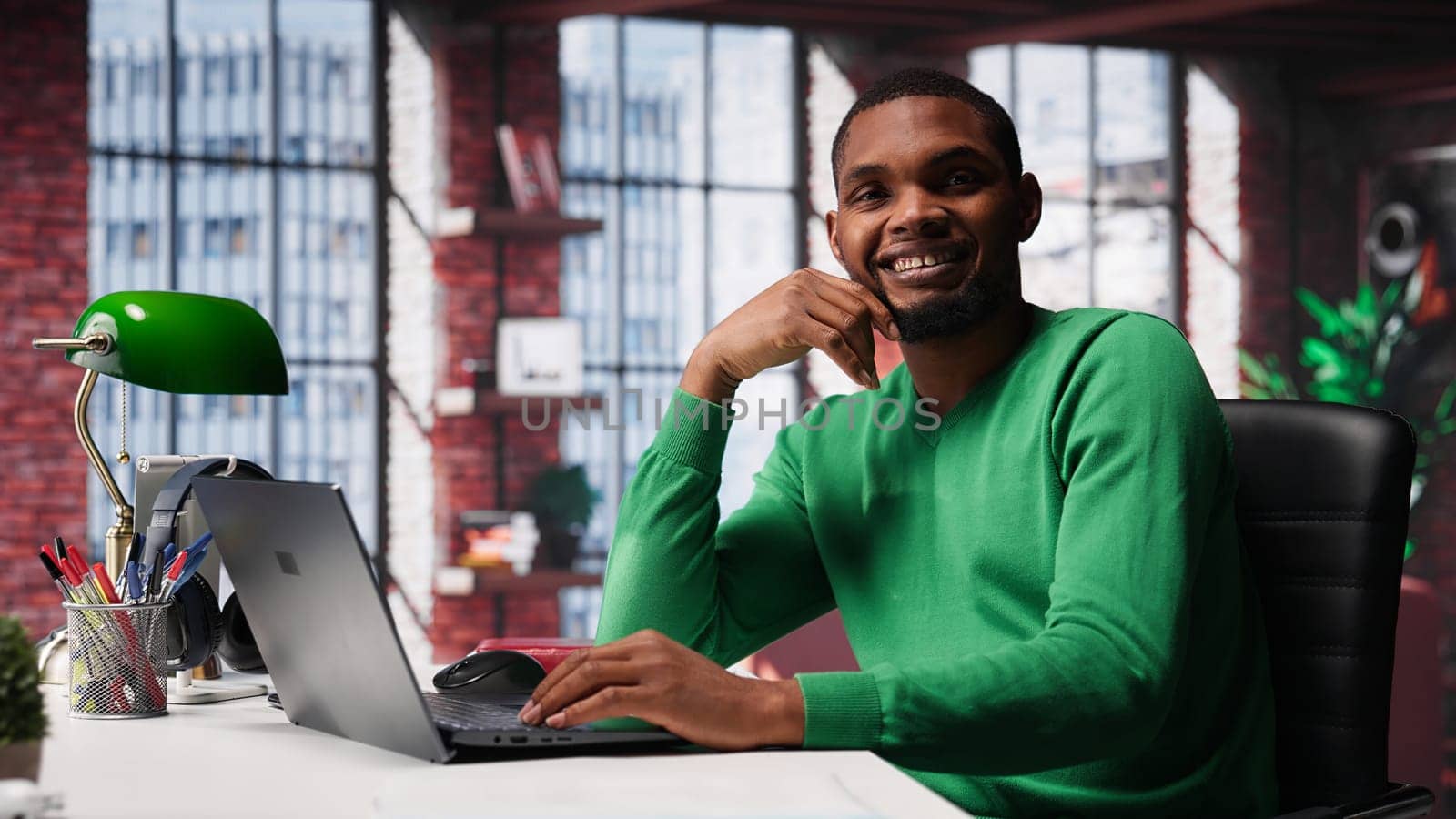 African american remote worker solving his daily freelancing tasks on laptop, working in relaxation from the comfort of his modern loft. Tech savvy black man internet user, multitasking. Camera A.