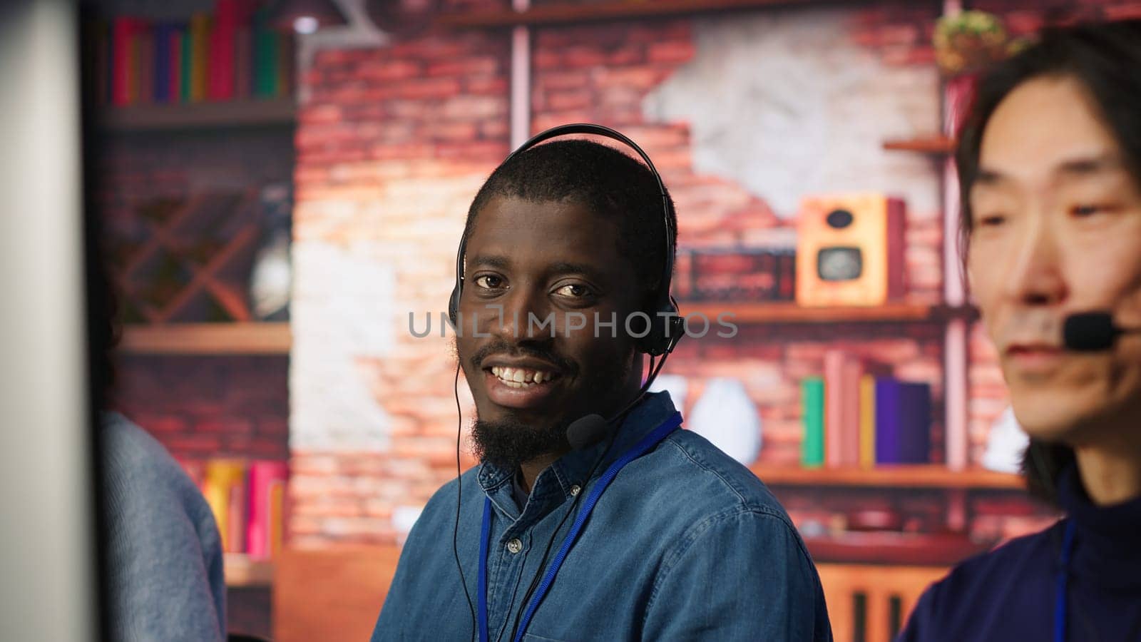 Portrait of smiling technical support specialist in call center office doing troubleshooting. Upbeat african american IT worker fixing customer connectivity issue, using headphones, camera A