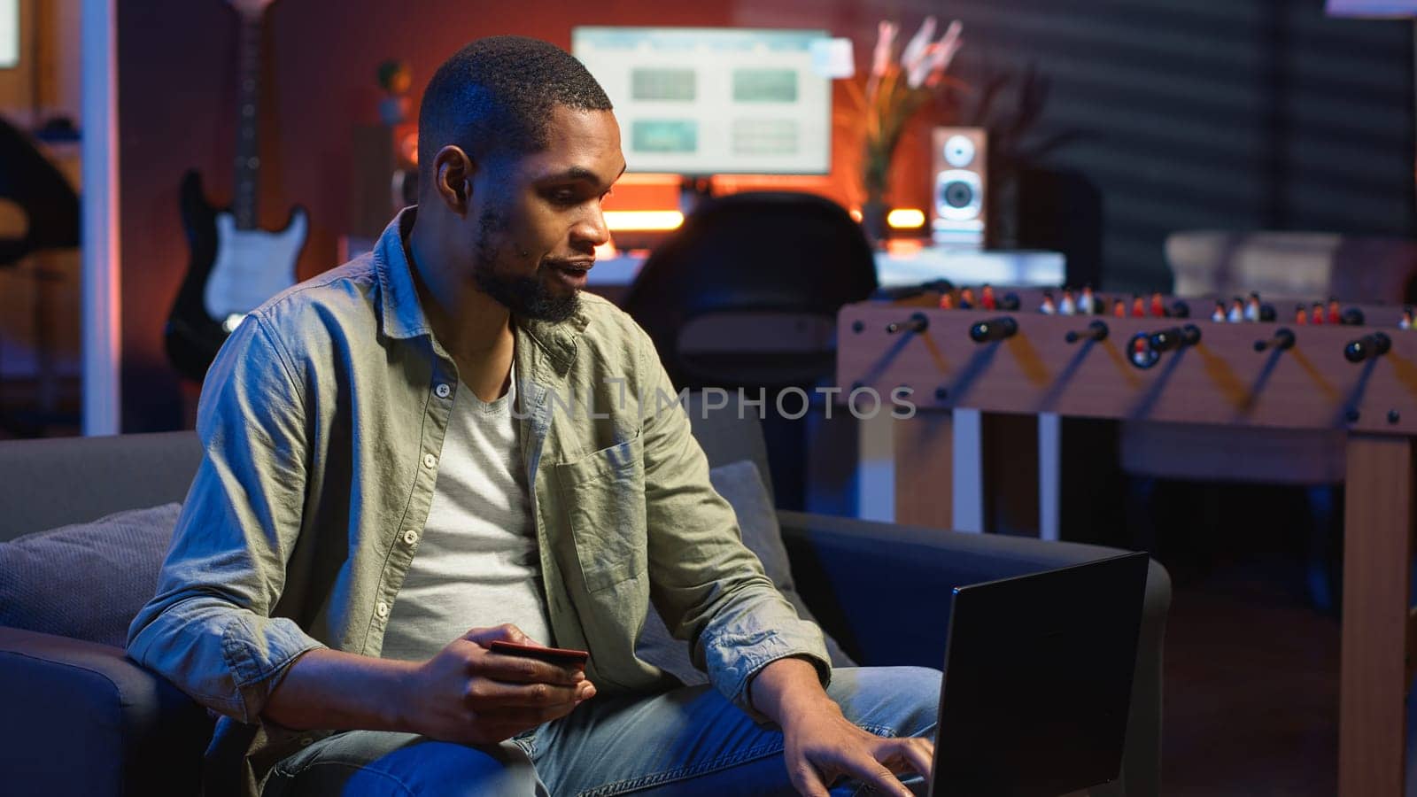 Young guy managing online banking and payments with the credit card, entering digits on website to confirm and oversee money transfer. Casual woman at home makes transactions. Camera B.